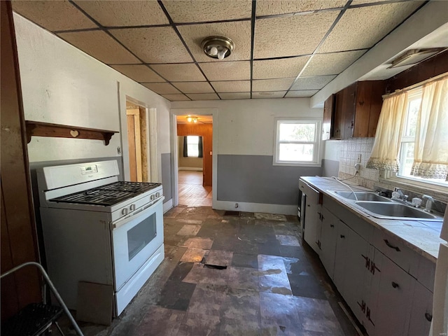 kitchen featuring backsplash, a drop ceiling, white gas range, and sink