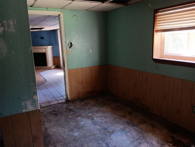 unfurnished room featuring concrete flooring, a paneled ceiling, and wooden walls