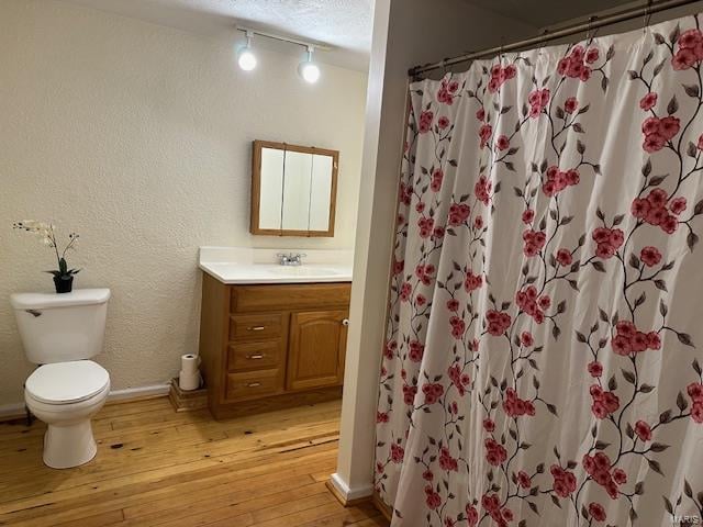 bathroom with walk in shower, wood-type flooring, a textured ceiling, toilet, and vanity