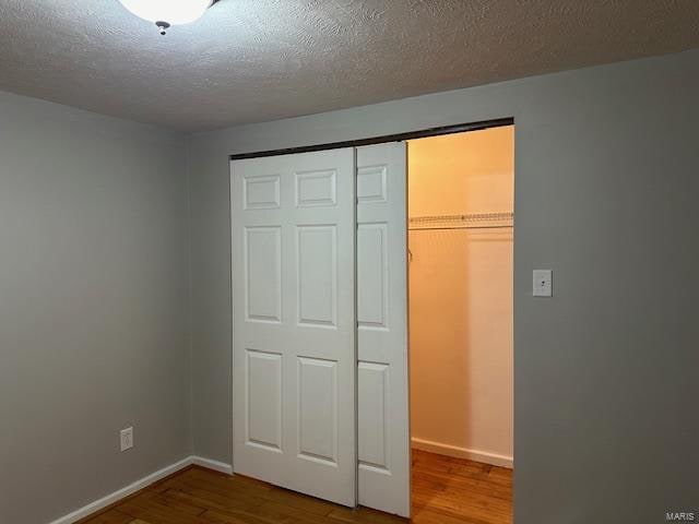 unfurnished bedroom featuring a closet, a textured ceiling, and hardwood / wood-style flooring