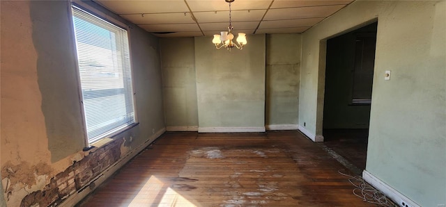 unfurnished dining area featuring a drop ceiling, dark wood-type flooring, and a chandelier