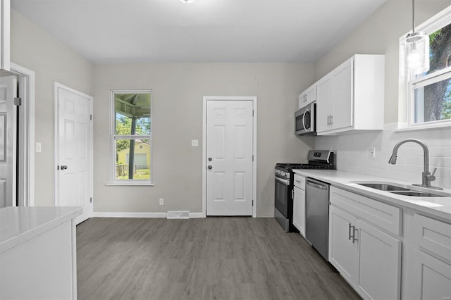 kitchen featuring sink, hanging light fixtures, appliances with stainless steel finishes, white cabinets, and hardwood / wood-style flooring