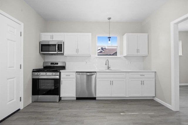 kitchen with white cabinets, sink, light hardwood / wood-style flooring, appliances with stainless steel finishes, and decorative light fixtures