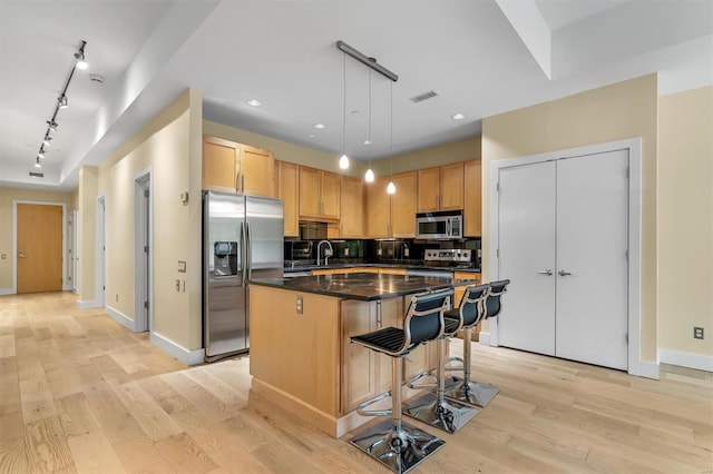 kitchen featuring light hardwood / wood-style flooring, appliances with stainless steel finishes, hanging light fixtures, tasteful backsplash, and a kitchen island