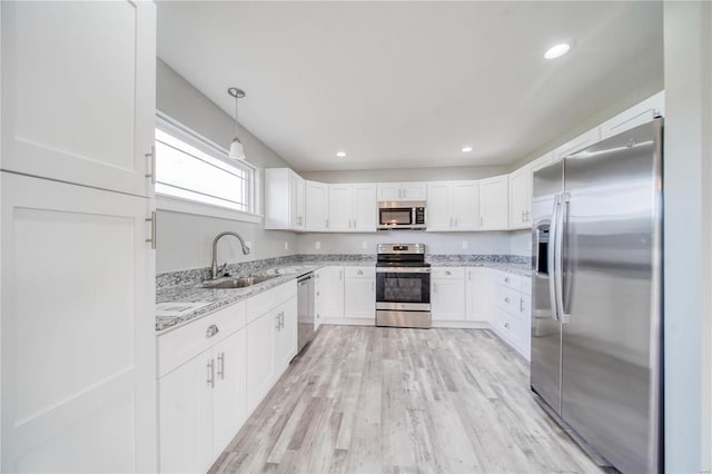 kitchen featuring white cabinets, stainless steel appliances, light hardwood / wood-style floors, light stone countertops, and sink