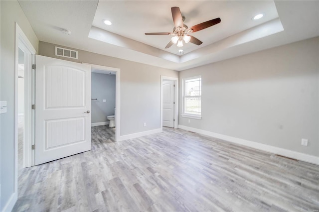 unfurnished bedroom featuring ensuite bathroom, ceiling fan, light hardwood / wood-style flooring, and a raised ceiling