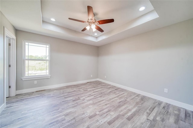 unfurnished room with light hardwood / wood-style floors, ceiling fan, and a raised ceiling