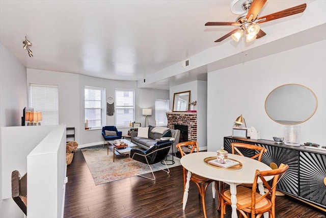 dining area with dark wood-type flooring, a brick fireplace, and ceiling fan