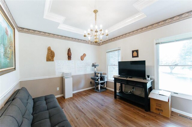 living room with an inviting chandelier, hardwood / wood-style floors, ornamental molding, and a raised ceiling