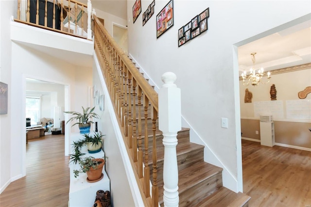 stairs with an inviting chandelier, crown molding, and hardwood / wood-style flooring