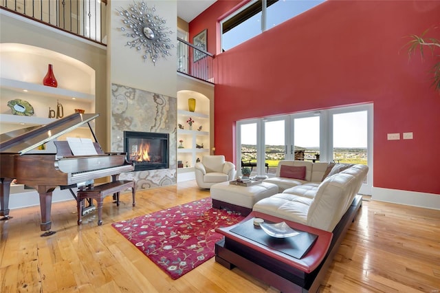 living room with built in shelves, a high end fireplace, hardwood / wood-style floors, and a high ceiling