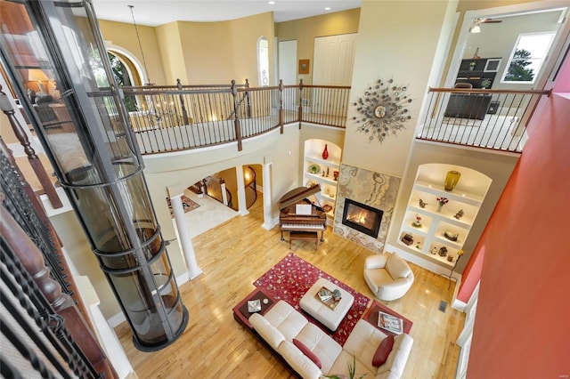 living room with a towering ceiling, a high end fireplace, hardwood / wood-style floors, and built in features