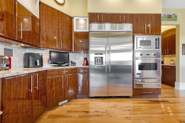 kitchen with light stone counters, built in appliances, decorative backsplash, and light wood-type flooring