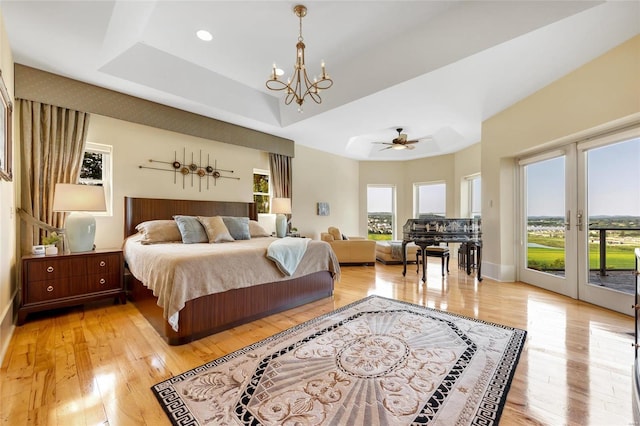 bedroom featuring access to exterior, light hardwood / wood-style floors, french doors, ceiling fan with notable chandelier, and a raised ceiling