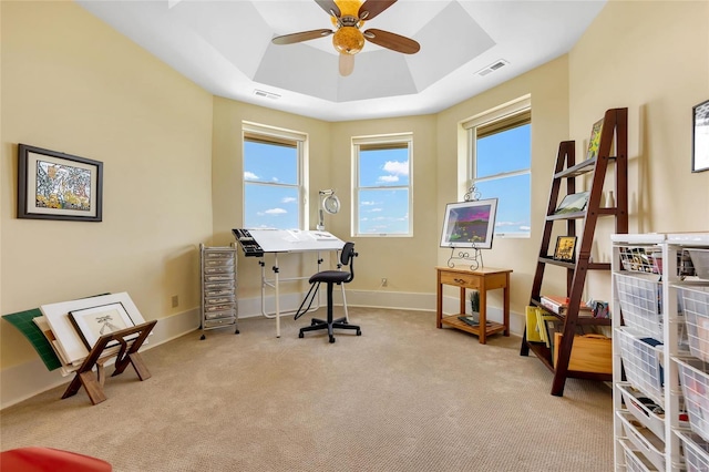 office area featuring ceiling fan, a tray ceiling, and light carpet