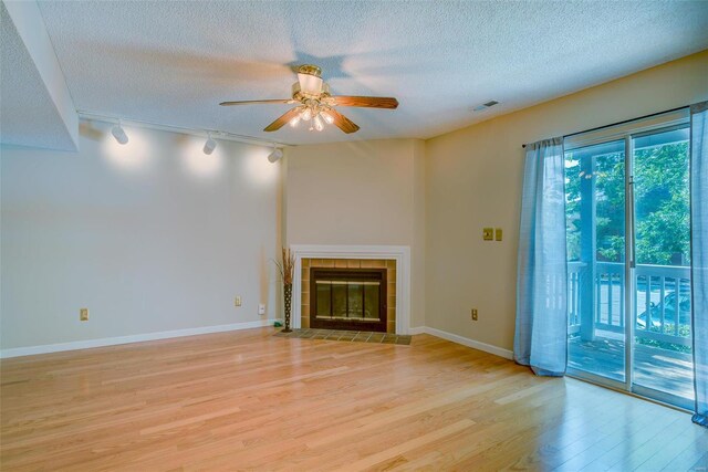 unfurnished living room with light wood-type flooring, track lighting, a tiled fireplace, a textured ceiling, and ceiling fan