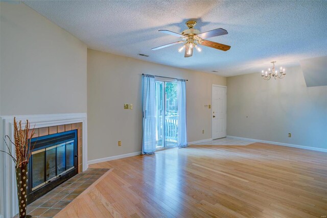 unfurnished living room with a tiled fireplace, ceiling fan with notable chandelier, hardwood / wood-style floors, and a textured ceiling