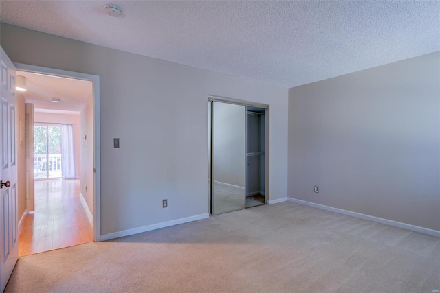 unfurnished bedroom featuring a textured ceiling, a closet, baseboards, and light colored carpet