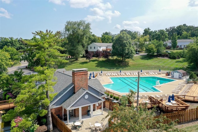 community pool with a patio, a lawn, an outdoor structure, and fence