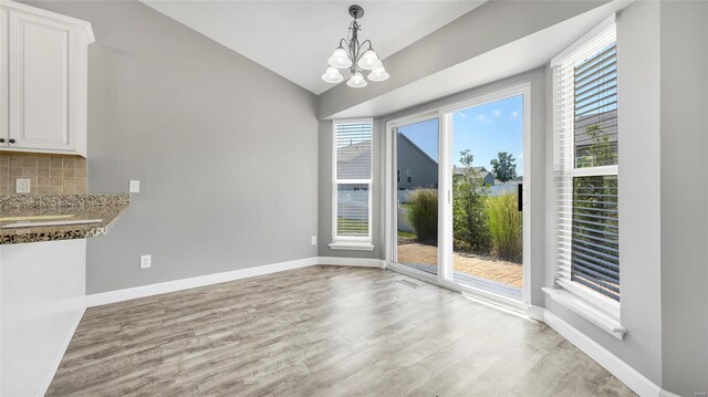 unfurnished dining area with light wood-type flooring, vaulted ceiling, and a notable chandelier