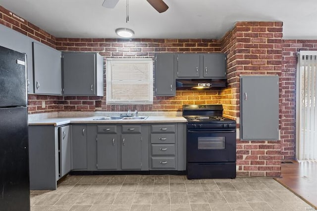 kitchen with black appliances, sink, ceiling fan, gray cabinets, and brick wall