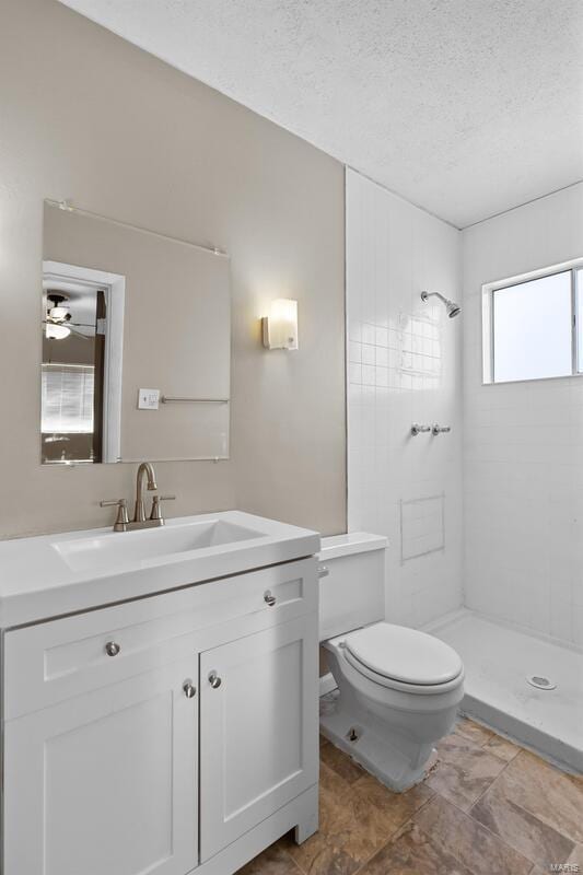 bathroom featuring vanity, a textured ceiling, tiled shower, and toilet