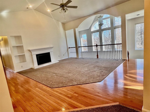 unfurnished living room featuring ceiling fan, wood-type flooring, high vaulted ceiling, and built in features