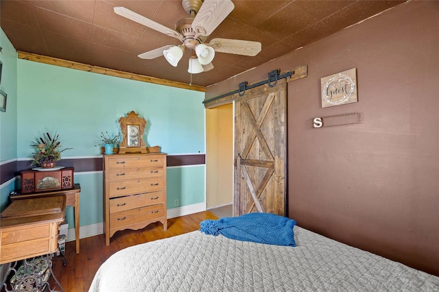 bedroom with ceiling fan, a barn door, and dark hardwood / wood-style flooring