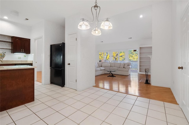 kitchen with light wood-type flooring, dark brown cabinets, decorative light fixtures, a notable chandelier, and black refrigerator