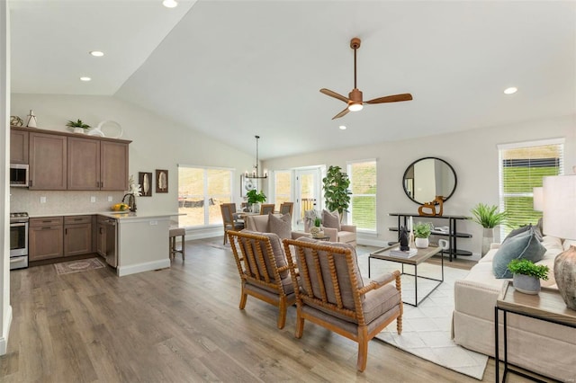 living room featuring sink, light hardwood / wood-style flooring, vaulted ceiling, and ceiling fan with notable chandelier