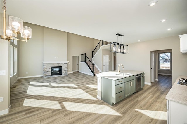 kitchen featuring sink, stainless steel dishwasher, light hardwood / wood-style floors, decorative light fixtures, and a center island with sink