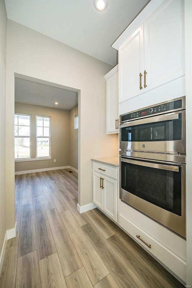 kitchen featuring light wood-type flooring, white cabinetry, and double oven