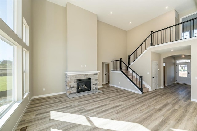 unfurnished living room featuring a fireplace, a towering ceiling, and light hardwood / wood-style floors