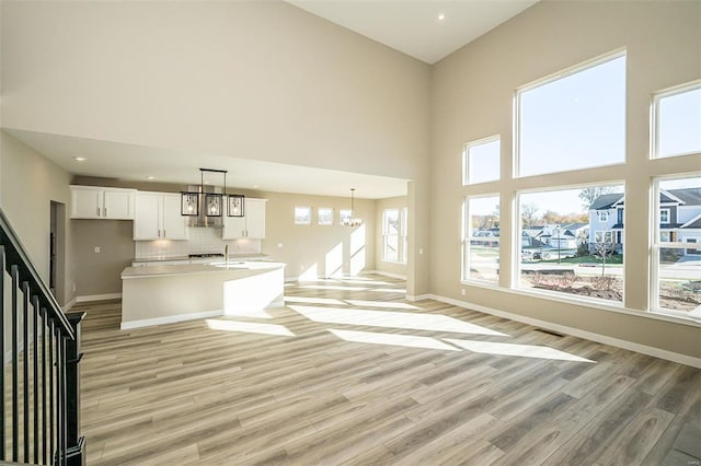 unfurnished living room with a chandelier, a towering ceiling, light wood-type flooring, and a wealth of natural light