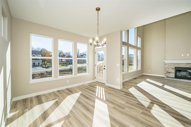 unfurnished dining area featuring a notable chandelier, plenty of natural light, light hardwood / wood-style floors, and a fireplace