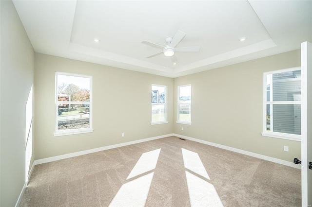 carpeted empty room with a raised ceiling, a wealth of natural light, and ceiling fan