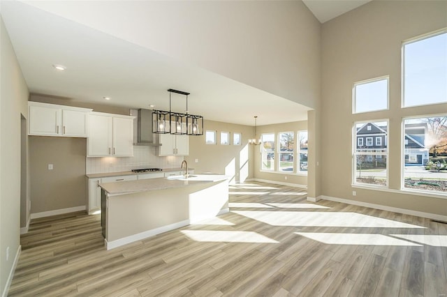 kitchen featuring sink, a chandelier, light hardwood / wood-style floors, white cabinetry, and an island with sink