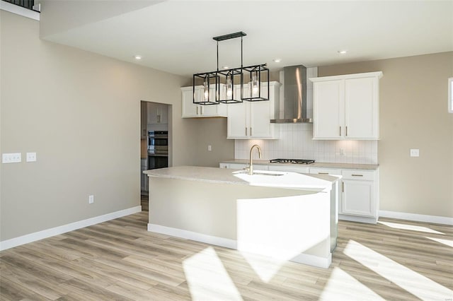 kitchen featuring sink, light hardwood / wood-style flooring, wall chimney exhaust hood, an island with sink, and white cabinetry