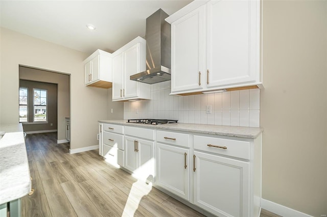 kitchen featuring white cabinets, light hardwood / wood-style flooring, wall chimney exhaust hood, and stainless steel gas cooktop