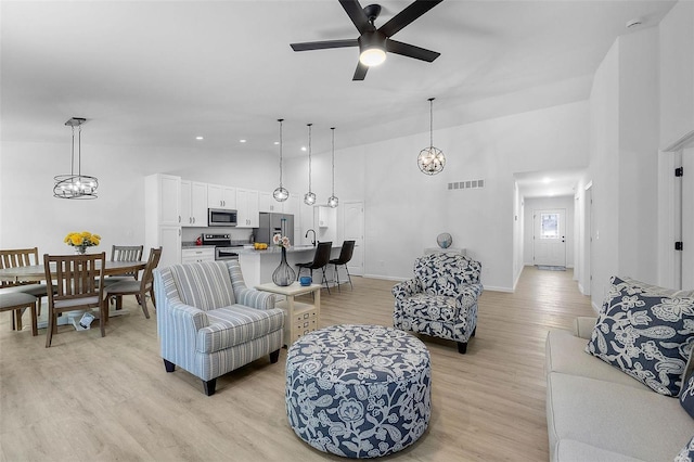 living room with ceiling fan with notable chandelier, sink, high vaulted ceiling, and light wood-type flooring