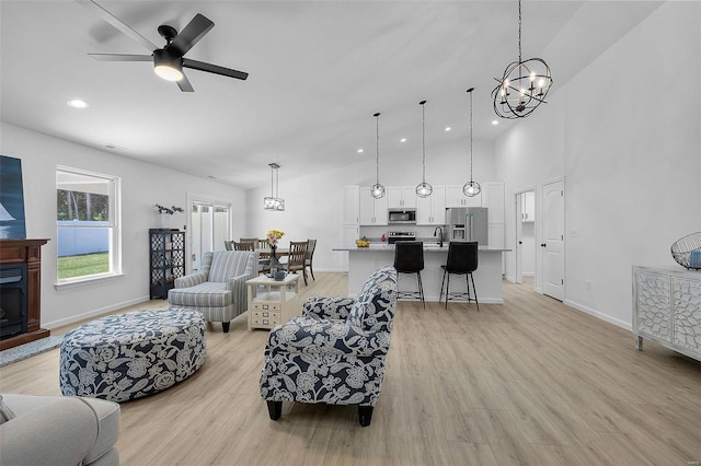 living room with high vaulted ceiling, sink, ceiling fan with notable chandelier, and light hardwood / wood-style floors