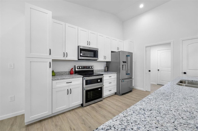 kitchen with stainless steel appliances, light stone countertops, white cabinets, and light hardwood / wood-style flooring