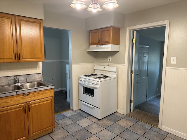 kitchen featuring white gas range, sink, light tile patterned flooring, and an inviting chandelier