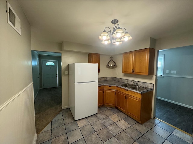 kitchen with white refrigerator, light colored carpet, an inviting chandelier, and sink