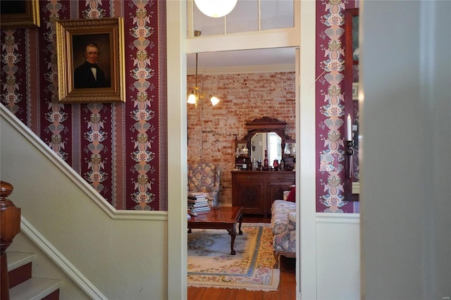 hall featuring hardwood / wood-style flooring, crown molding, and brick wall