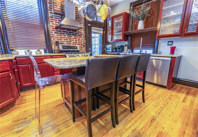 interior space with stainless steel dishwasher, light wood-type flooring, a kitchen island, and wall chimney exhaust hood