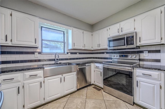 kitchen with sink, white cabinetry, light tile patterned floors, dark stone countertops, and appliances with stainless steel finishes