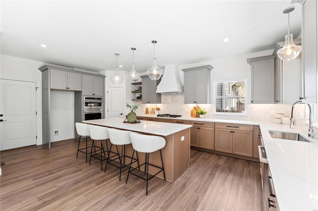 kitchen with appliances with stainless steel finishes, premium range hood, wood-type flooring, sink, and a center island