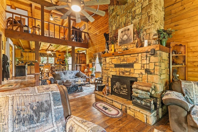 living area with hardwood / wood-style flooring, ceiling fan, a stone fireplace, wood walls, and high vaulted ceiling