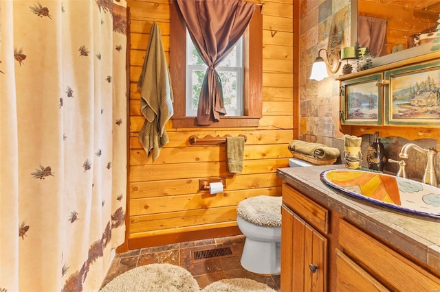 bathroom featuring toilet, wood walls, vanity, and visible vents